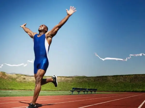 A man running on the track with his arms in the air.