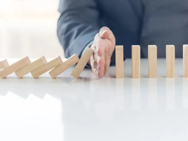 A person stopping the domino effect on a table.