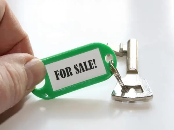 A person holding up a key with the word for sale on it.
